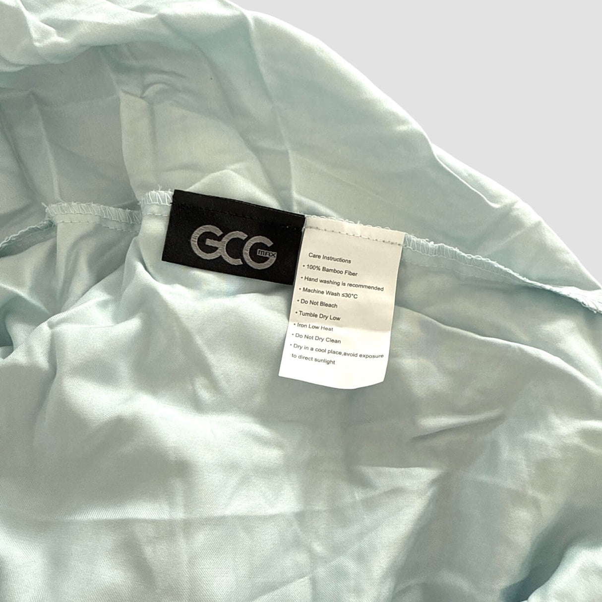 Lyseblåt GCG MAX bambus lagen med mærker, der viser vaskeanvisninger og produktinformation.