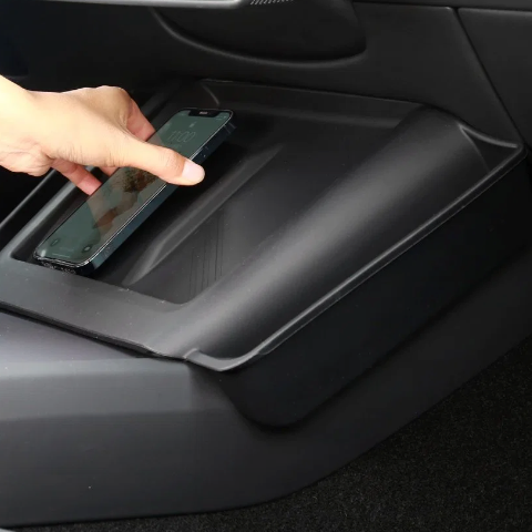 En hånd lægger en telefon på det sorte cover til den trådløse oplader i en Tesla Model 3 Highland