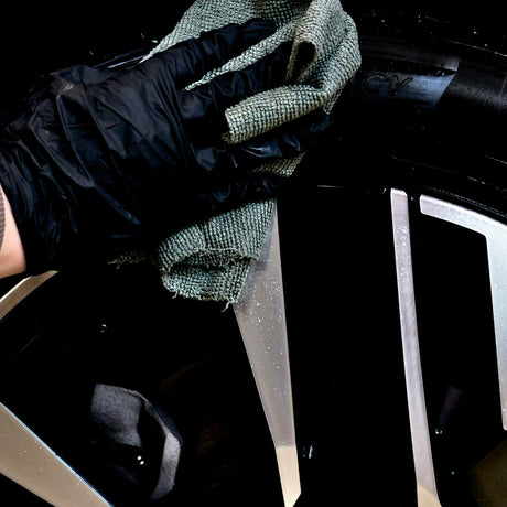 Hånd med handske påfører Autoland dækglans på et bildæk med en klud.