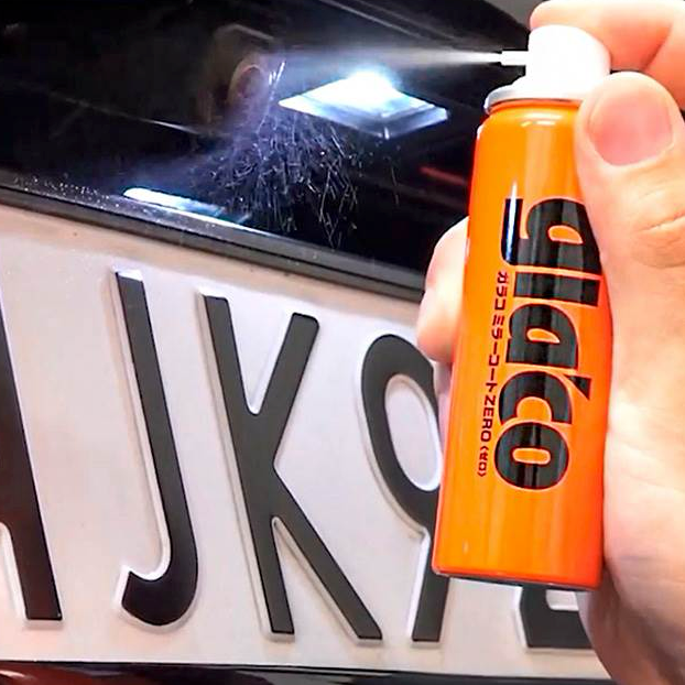 Hånd der sprayer Glaco Mirror Coat Zero på et bilkamera over nummerpladen.