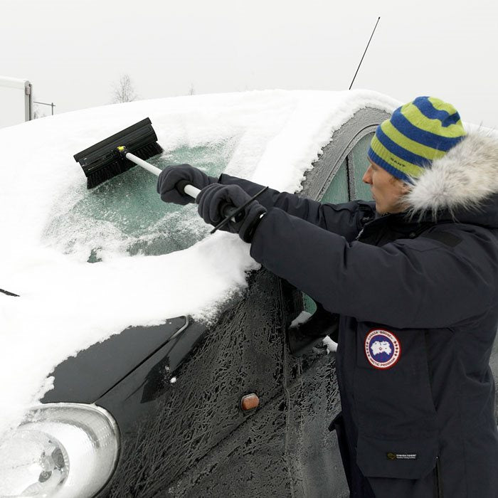 Mand som skraber sne af forruden på en bil