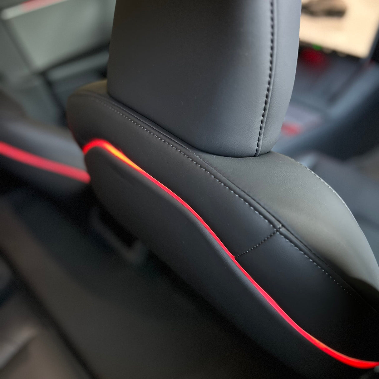 Rødt ambientelys langs plastikryglænet på forsæderne i en Tesla Model 3 Highland, set tæt på